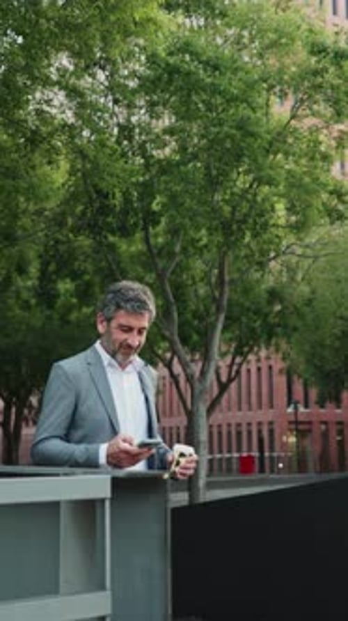 Man Uses Phone and Sips Coffee in City