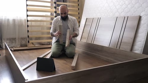 Man Assembling Bed Frame Using Tablet Instructions