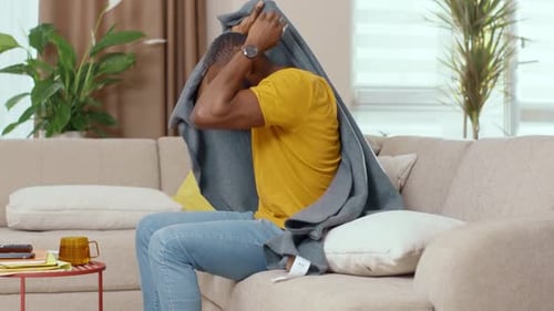 Jeune homme afro-américain en mauvaise santé recouvert d'une couverture pour se réchauffer en restant à la maison et souffrant de fièvre