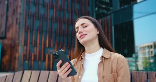 Distressed woman looking at phone on city bench