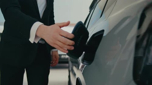 Camera Focus on Person in Black Suit and White Shirt Opening Charging Dock on Side of Vehicle Label