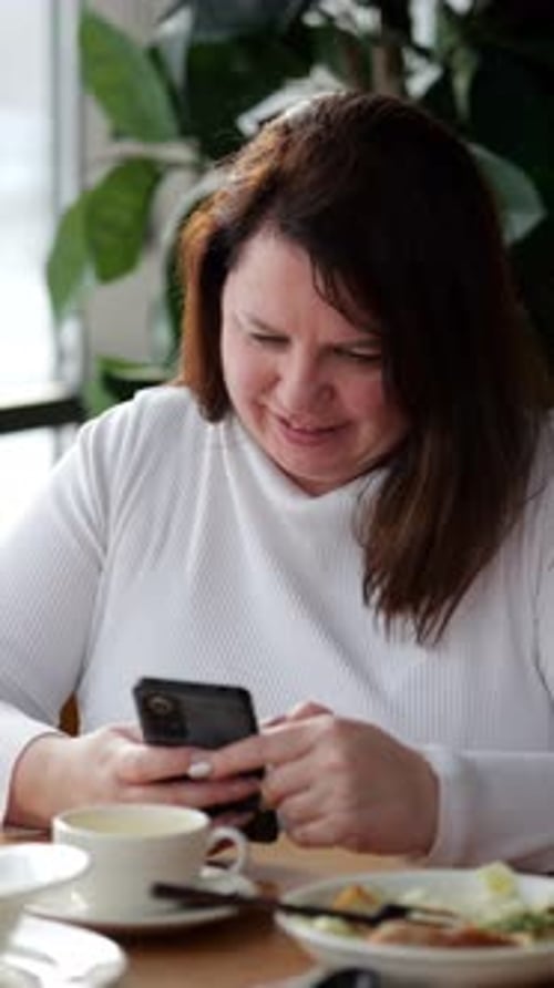 Mujer que usa un teléfono inteligente mientras desayuna en un café