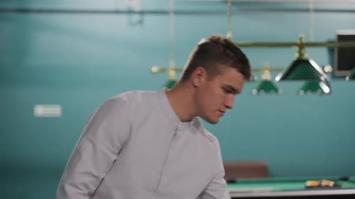 Man in White Shirt Tossing Billiard Ball in Stylish Pool Hall with Green Tables