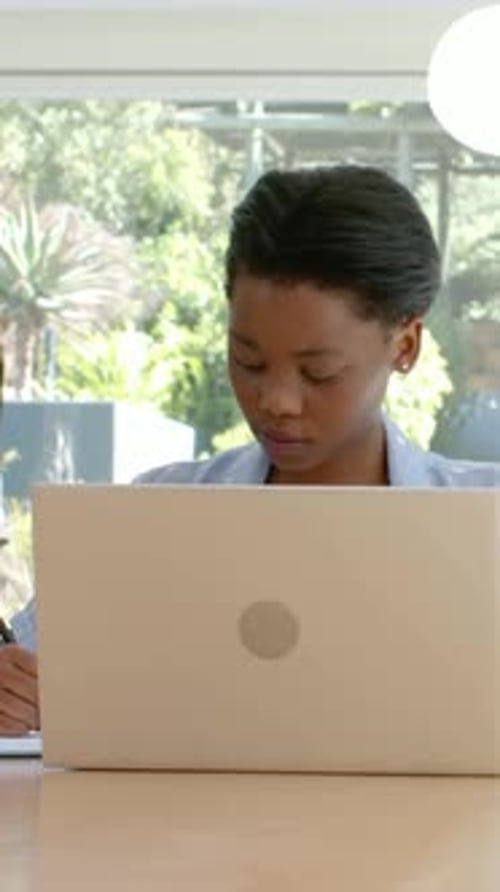 Vertical video: Reading laptop screen for study, woman in light blazer noting at home, pen notebook