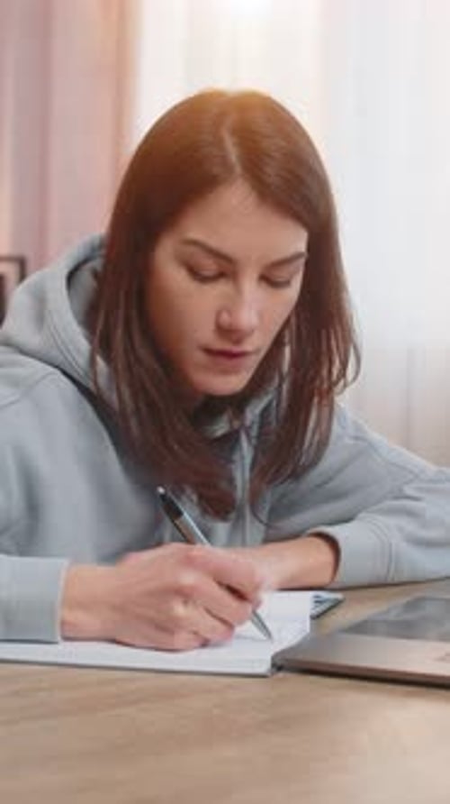 Woman Writes in Notebook with Laptop at Desk Indoors