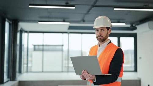 Confident Engineer in an Office Building Uses Laptop for Construction Project