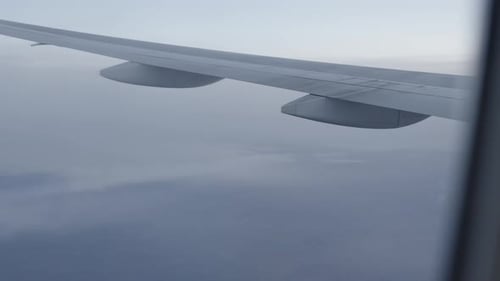 Aerial view from airplane window, wing over clouds at high altitude, tranquil sky