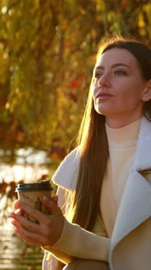 Beautiful thoughtful lady with a paper cup in her hands sitting near the river.