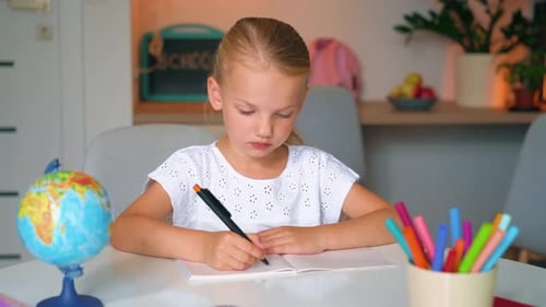 Child Kid Girl doing her homework art a desk. School girl writes in a notebook.