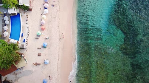 Tropischer Strand mit Sonnenschirmen und türkisfarbenem Meerblick von oben nach unten auf Bali