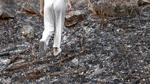 The Woman's White Attire Stands Out Against the Backdrop of the Burnt Forest As She Treads Upon the