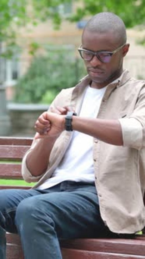 Vertical Video, Young African Man Checking Wrist Watch on Park Bench