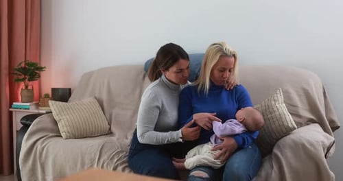 Two Women Cradling Infant on Couch Indoors