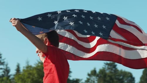 Enthusiastic boy holding large American flag outdoors
