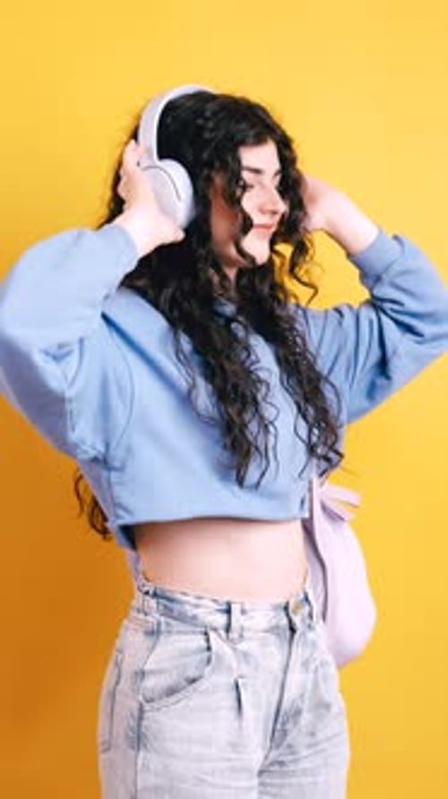 Young Happy Woman Listening to Music and Dancing on Yellow Background Vertical