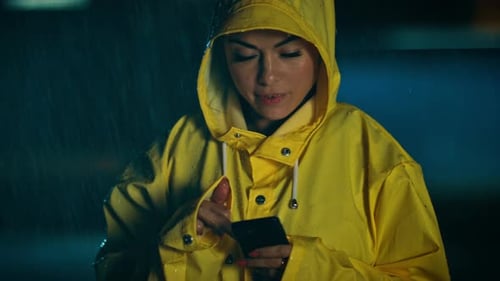 Woman in yellow raincoat uses phone in rain