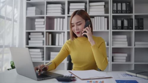 Businesswoman is talking to clients and colleague on the phone and working on laptop in office