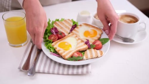 Frau legt frisch zubereiteten Eierloch-Toast mit einer Tasse frischen heißen Espresso-Kaffees auf den Tisch