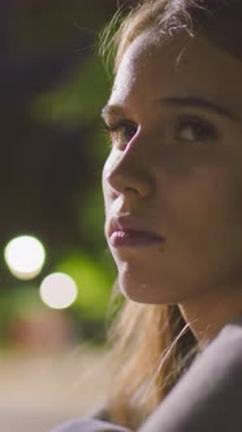 Femme attentionnée illuminée par les lumières du parc dans un reflet nocturne silencieux