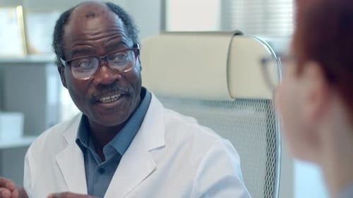 Senior Clinician Speaking with Coworker at Meeting in Medical Office