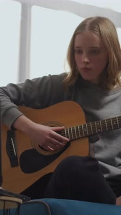 Teenage Girl Practicing Acoustic Guitar at Home While Watching an Online Lesson on Laptop Focusing