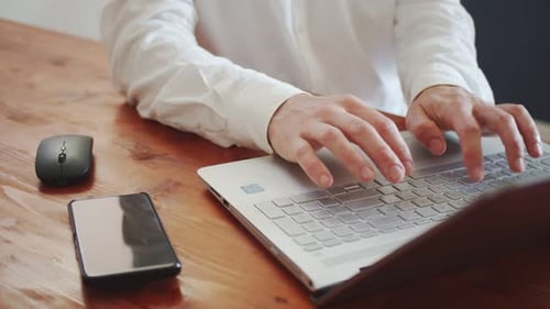 A Young Adult Man in a White Shirt Works on a Laptop There is a Smartphone Nearby View From Above