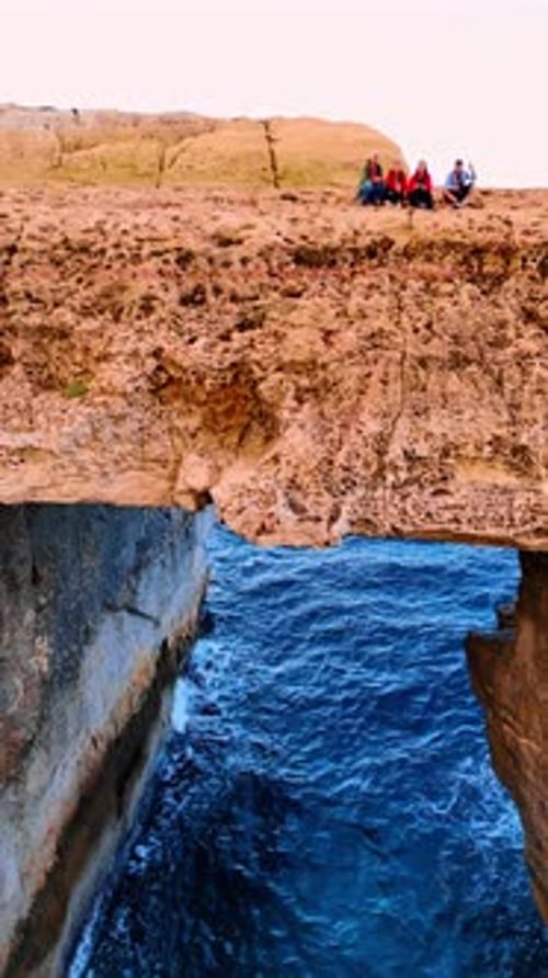 People sit on the bare rock at the shore of the Mediterranean Sea. Coast of Malta, Europe