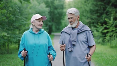 Old american grandparents enjoy nordic walking wood park. Elderly people stroll.