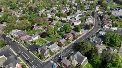 Aerial approaching shot of american downtown with cars on junction. Spring season with green trees a