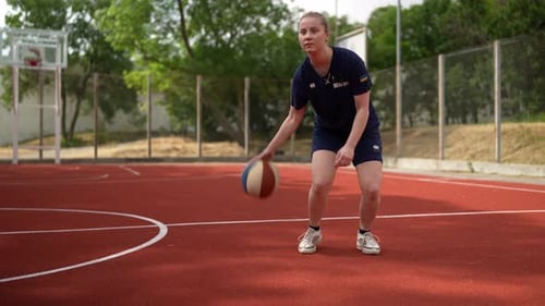 A Happy and Confident Girl Basketball Player in a Blue Sports Uniform Plays Basketball and Dribbles