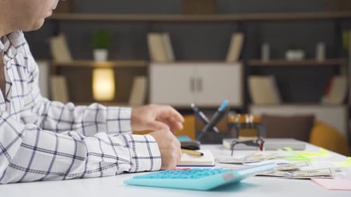Man Calculates Finances at Desk with Calculator