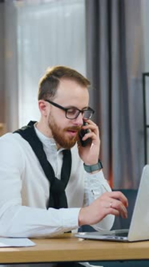 Man Works At Laptop While Talking on Phone