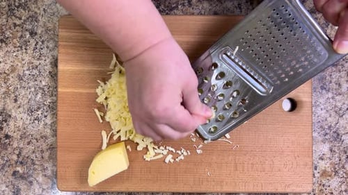 Hartkäse auf einer großen Metallreibe gegen ein Holzbrett reiben. Ansicht von oben.