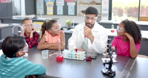 In a school classroom, a biracial male teacher demonstrates a science experiment