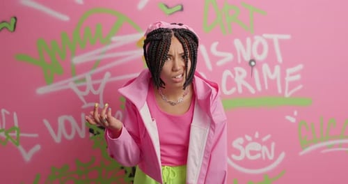 Stylish woman in pink jacket poses against graffiti wall
