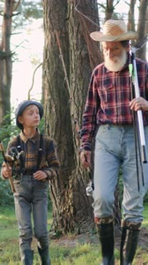 Boy and Senior Man Walk With Fishing Poles in Woods