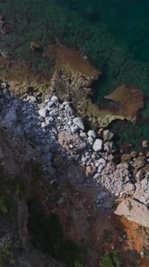 Vertical Video of a Scenic Rocky Beach With Gentle Waves Washing Over Smooth Stones Under the Bright