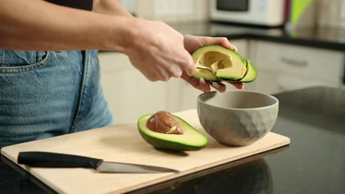 Person Scooping Avocado with Spoon into Bowl