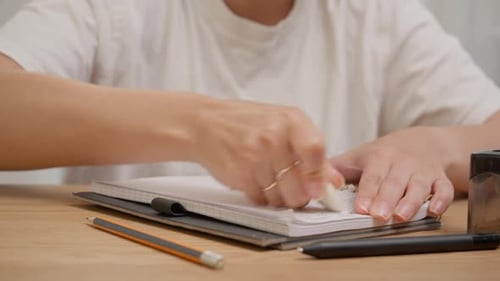 Female hand erasing pencil marks in spiral notebook with white eraser and audio