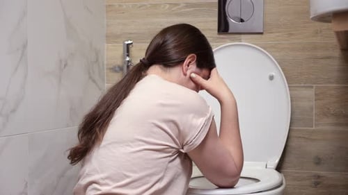 Woman Feels Nauseous Sitting Near Toilet in Bathroom