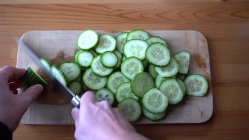 Man chef cutting cucumber on chopping wooden board