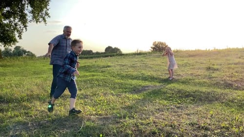 Grandfather Runs with Grandchildren Through Grassy Field