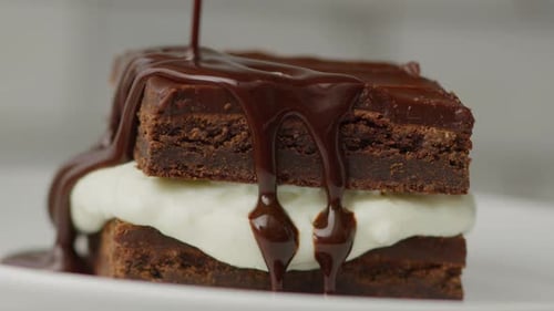 Chocolate Sauce Being Poured on Cream-Filled Brownie