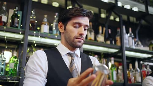 4K Male bartender preparing alcoholic drink in cocktail shaker at restaurant bar.