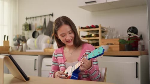 Smiling Woman Plays Ukulele at Kitchen Table
