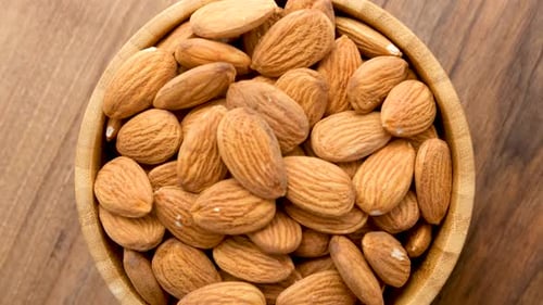 Close Up View Of A Wooden Bowl Filled With Peeled Almonds Rotates On A Wooden Surface