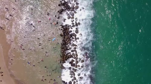 Tropischer Strand mit Menschen, die das ruhige Wasser hinter einem Wellenbrecher genießen