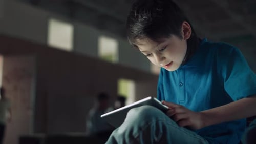 Excited Playful Teen Boy Playing Online Game Holding Tablet in School Hall