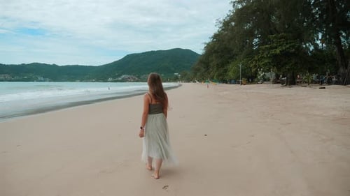 Woman Walks Alone on Sandy Beach During Daytime Enjoying Serene