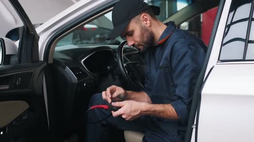 On the seat, with digital tablet. Mechanic working in a car service station.